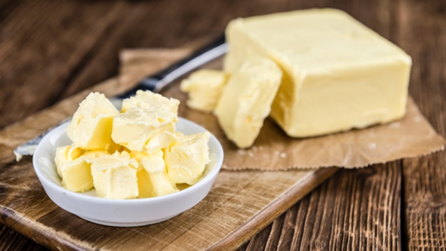 Rectangular block of butter on a white plate with a butter knife beside it.