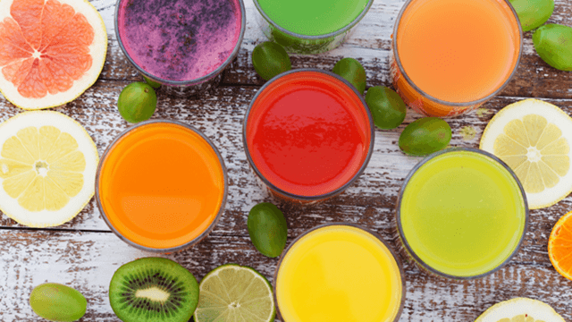 Top view of assorted colorful fresh fruit juices in glasses surrounded by sliced citrus fruits, kiwi, and green grapes on rustic wooden table